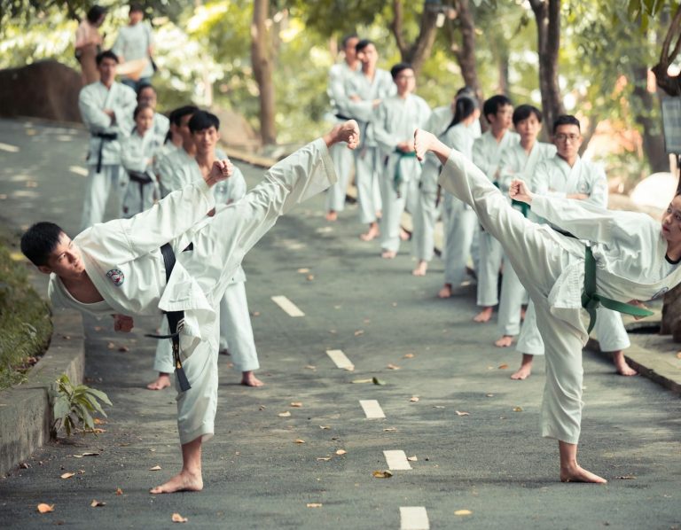 Gruppentraining von Taekwondo, die hohe Tritte auf einer Straße ausführen.
