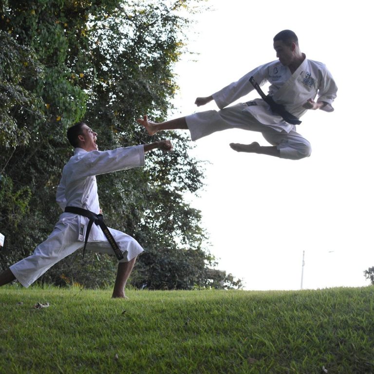 Zwei Taekwondo Kämpfer in Aktion: Einer springt mit einem Kick, der andere bereitet sich vor.